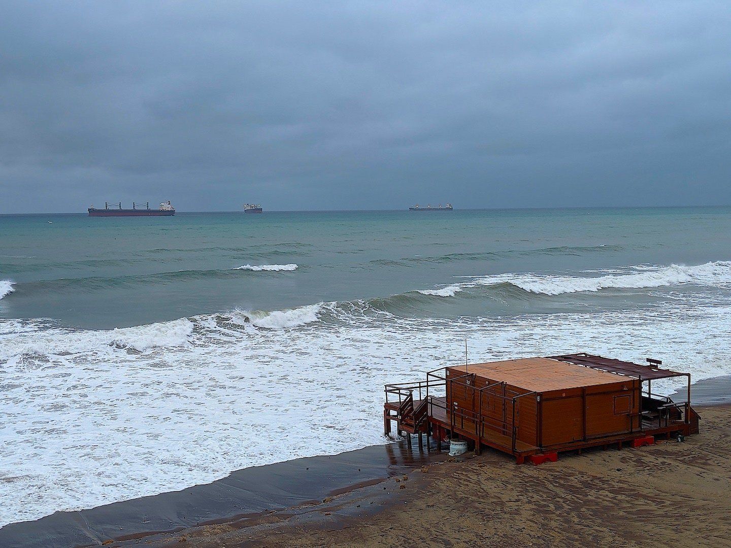 looking down from above onto the beach below where the storm is making the waves surround a wooden beach bar