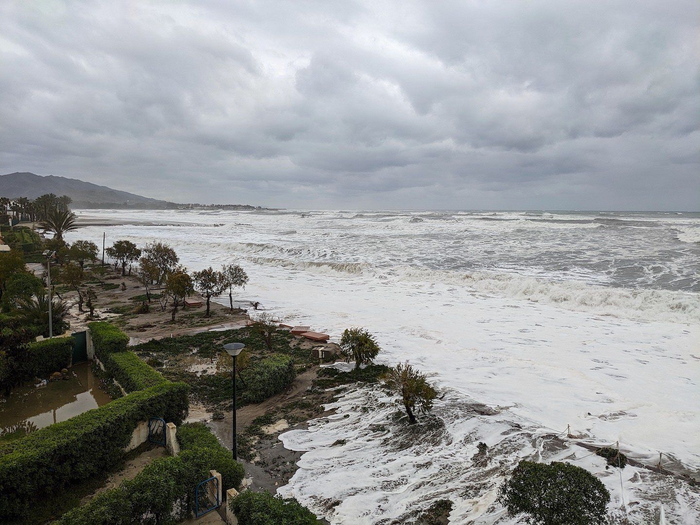 Beach with large waves and flooding in gardens by buildings