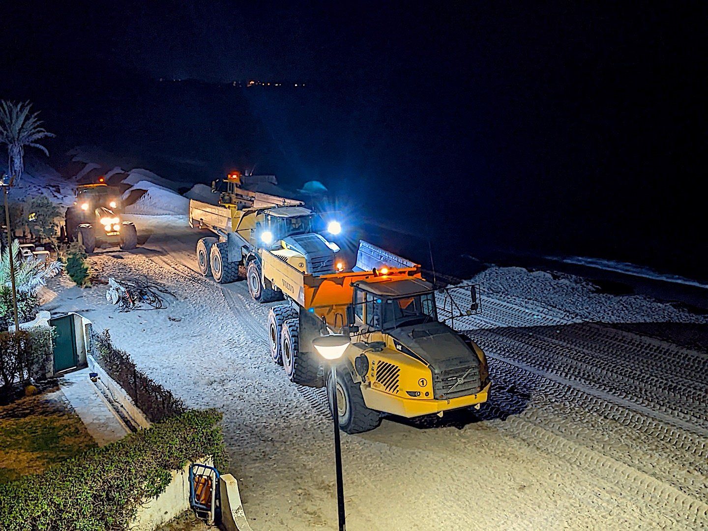 two trucks and a tractor working on a beach at night