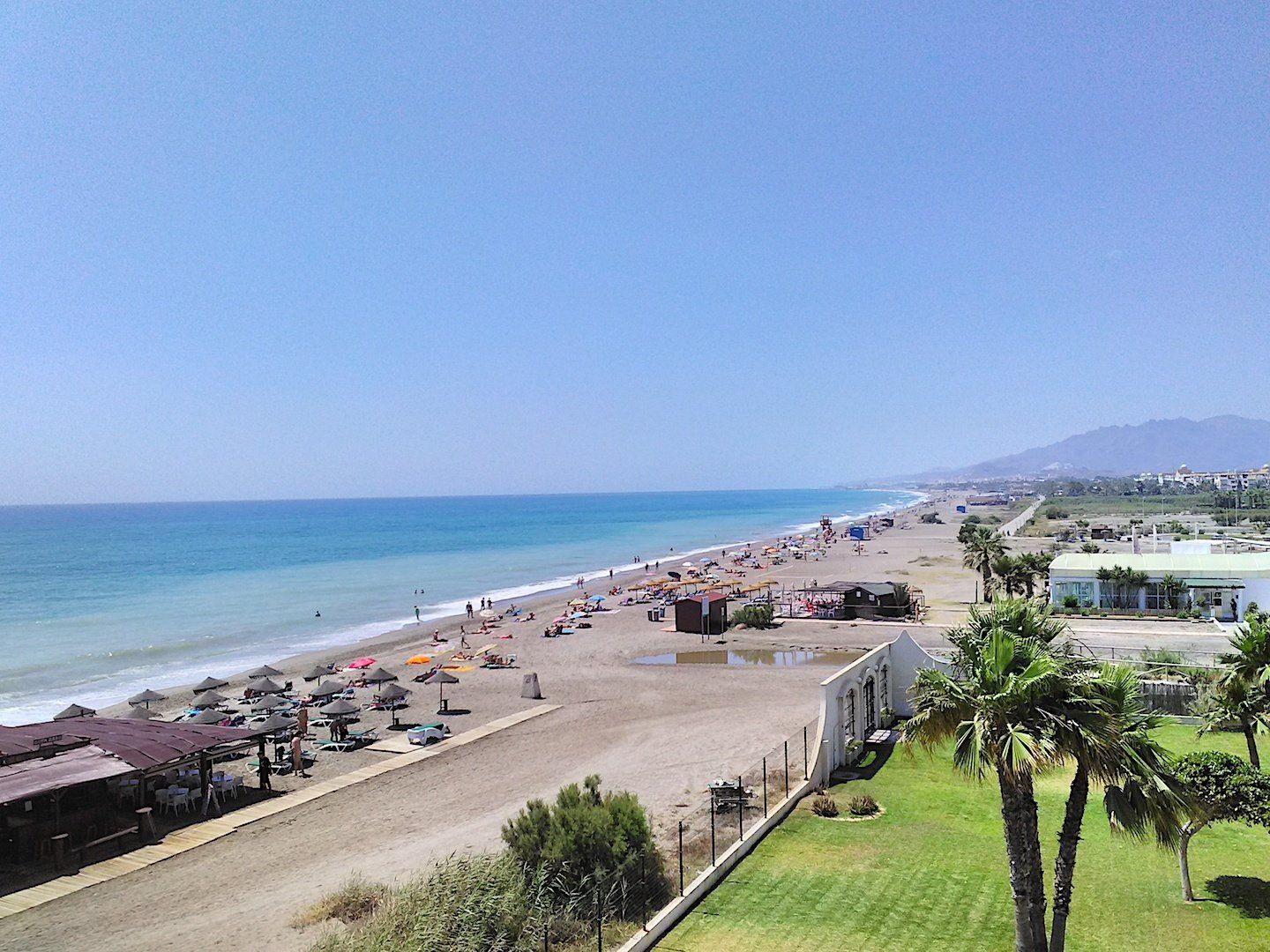 a view taken from above of the beach looking south and on the shoreline all you can see is lots of coloured parasols