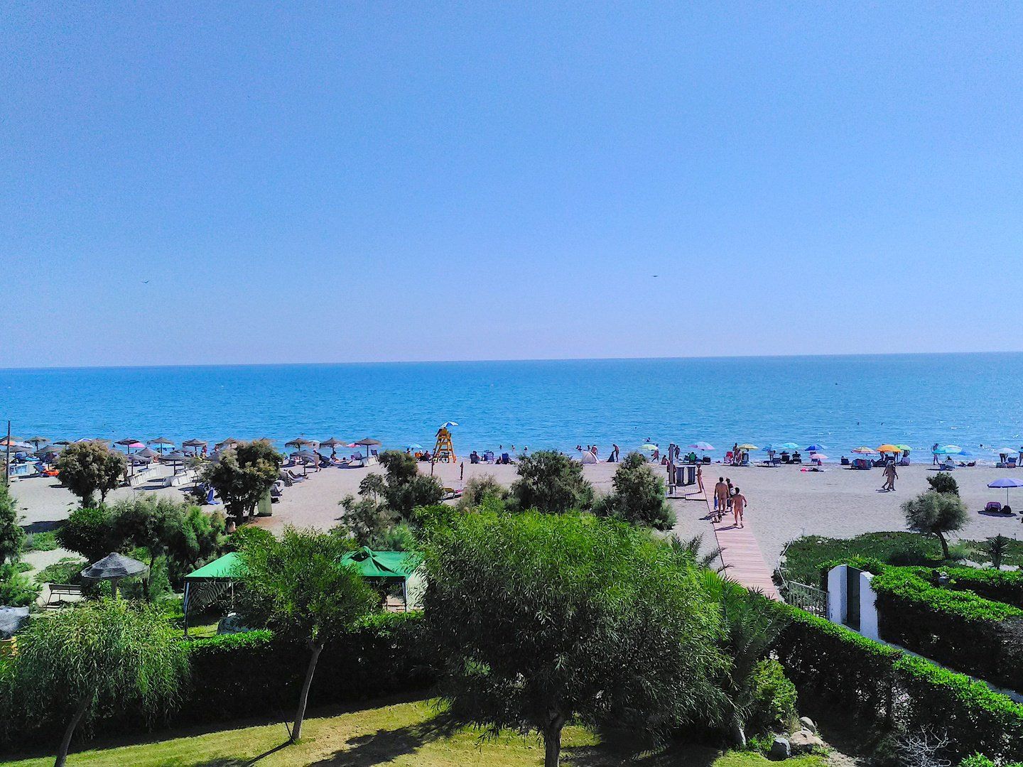 view from the terrace looking across the naturist beach where people are walking naked down the path onto the beach