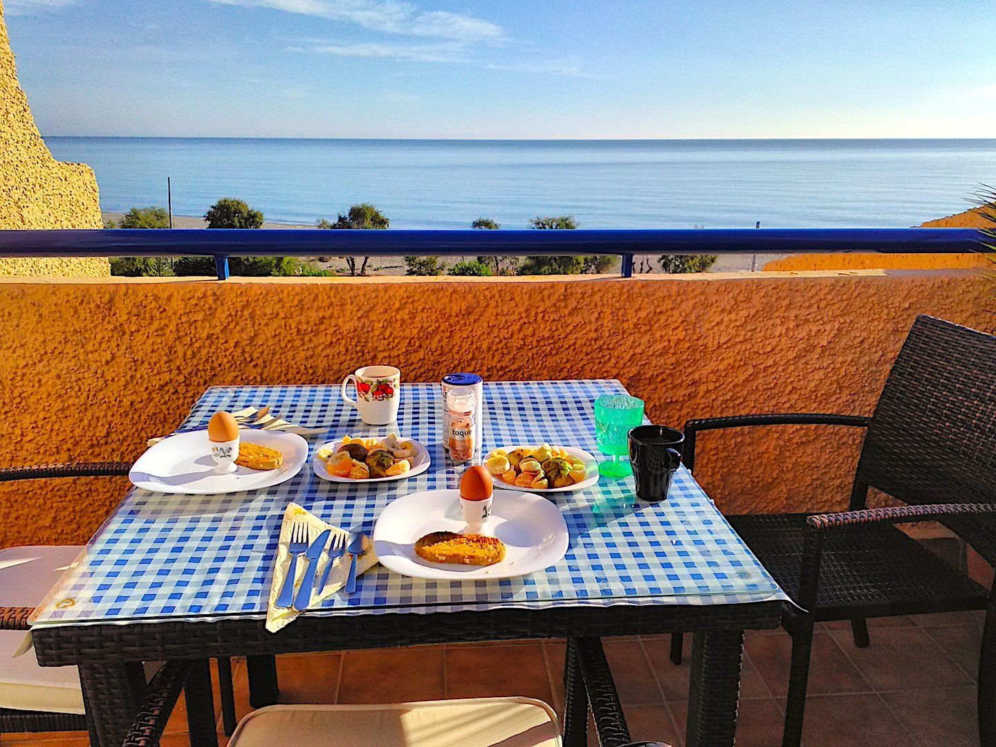 table with check blue and white cloth spread with a breakfast feast and a fabulous sea view