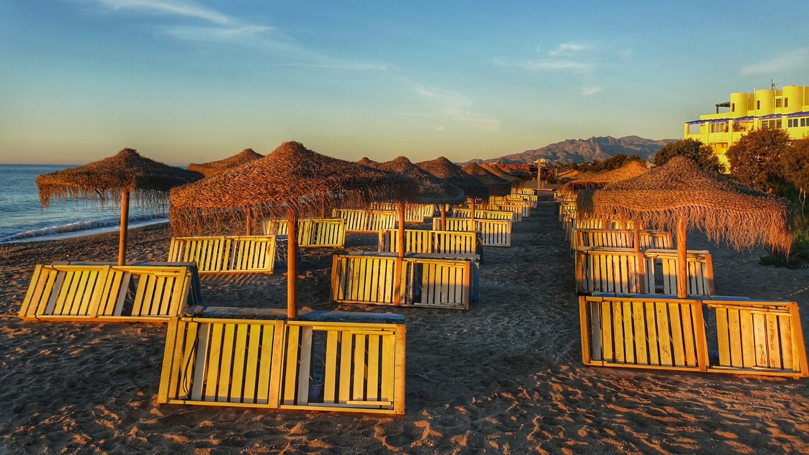 three rows of sun beds turned on their sides leaning against the parasols while the dawn sun shines on them