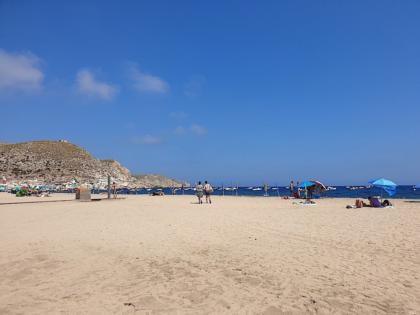 a wide golden sandy wild beach with blue skies and seas and some people in the distance