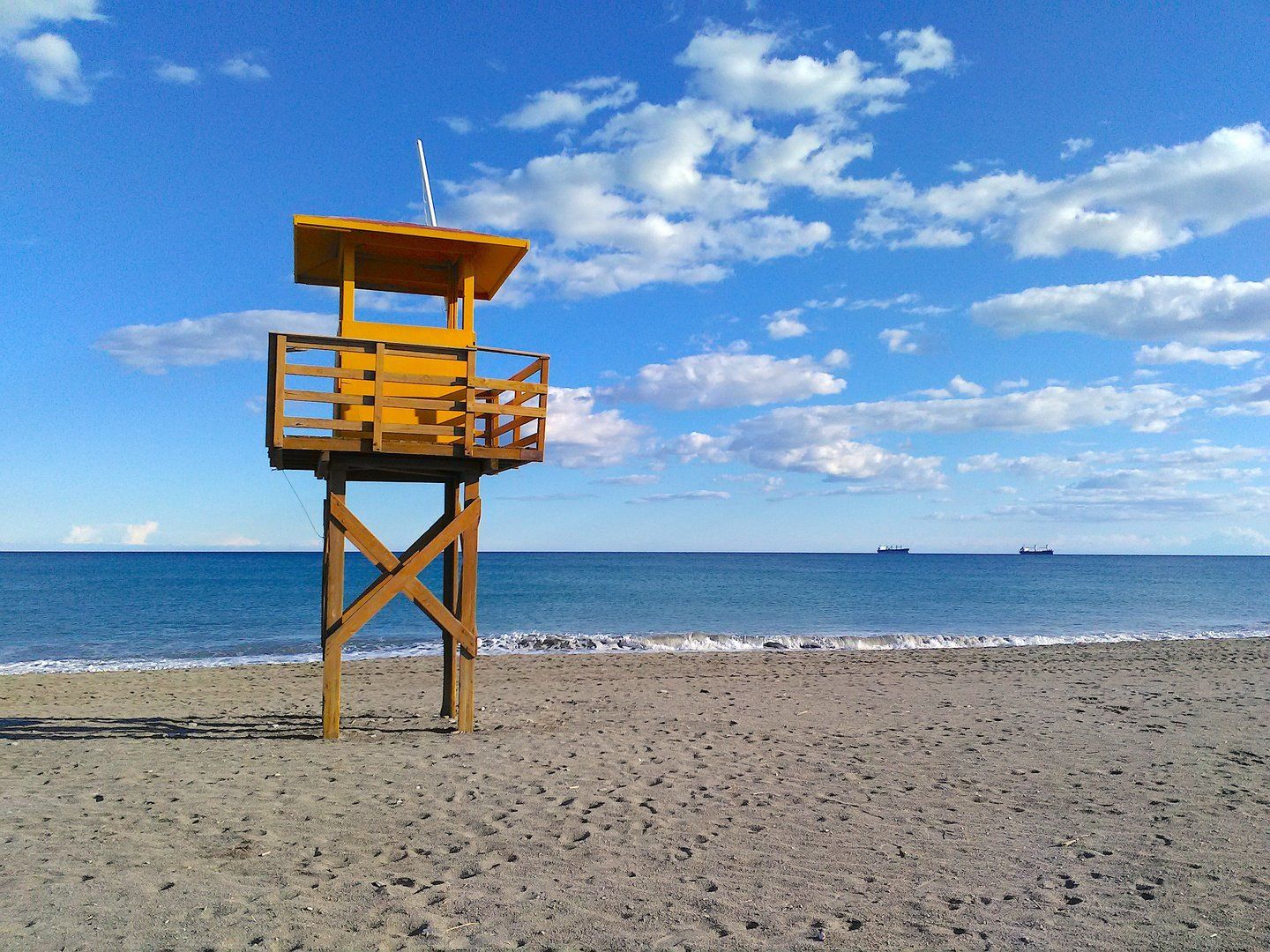 a lonely looking lifeguard tower but the sea looks calm and there are two ships on the horizon