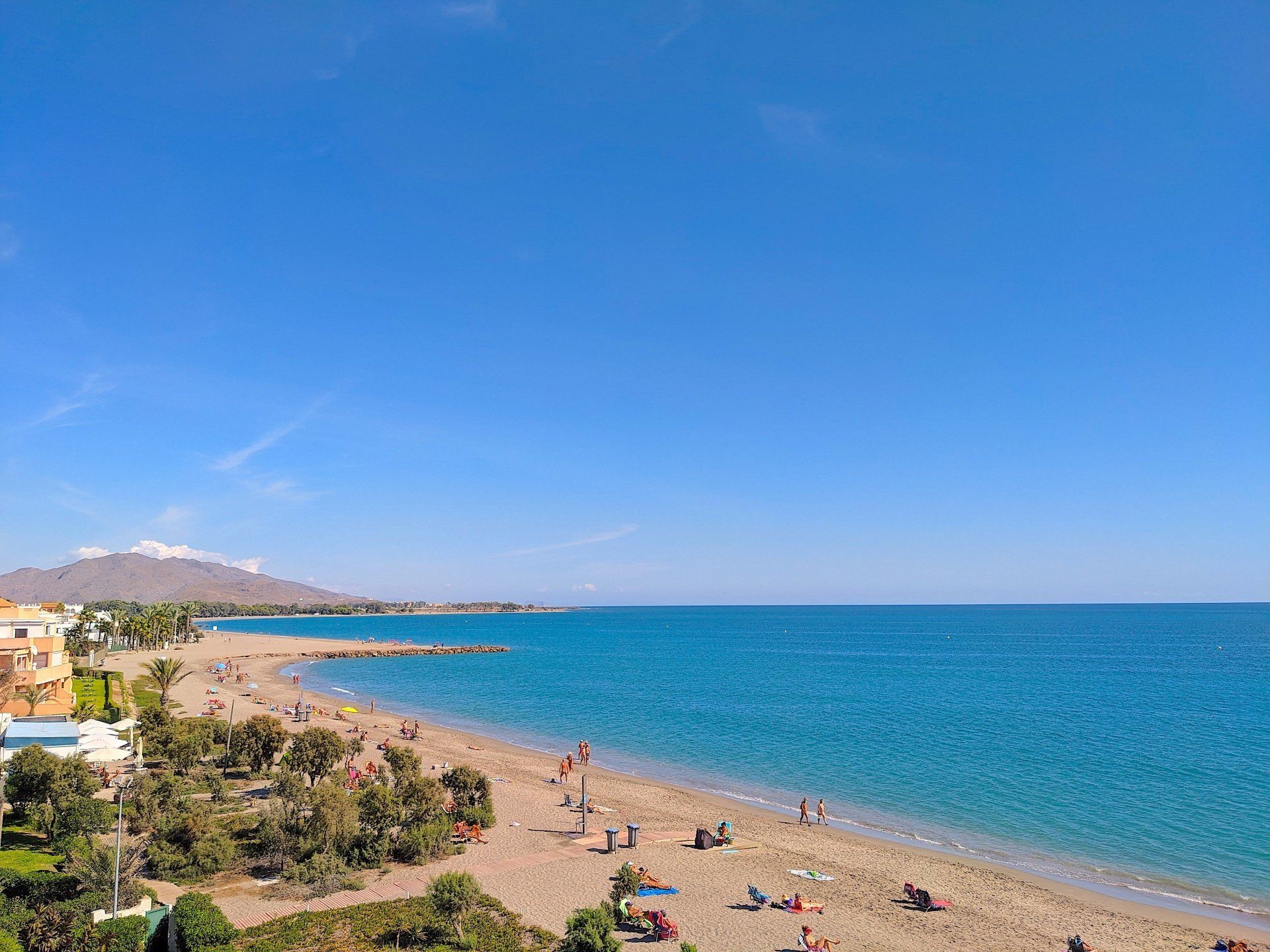 the sandy beach stretched north and the sea and sky are blue and there are people sunbathing on the beach