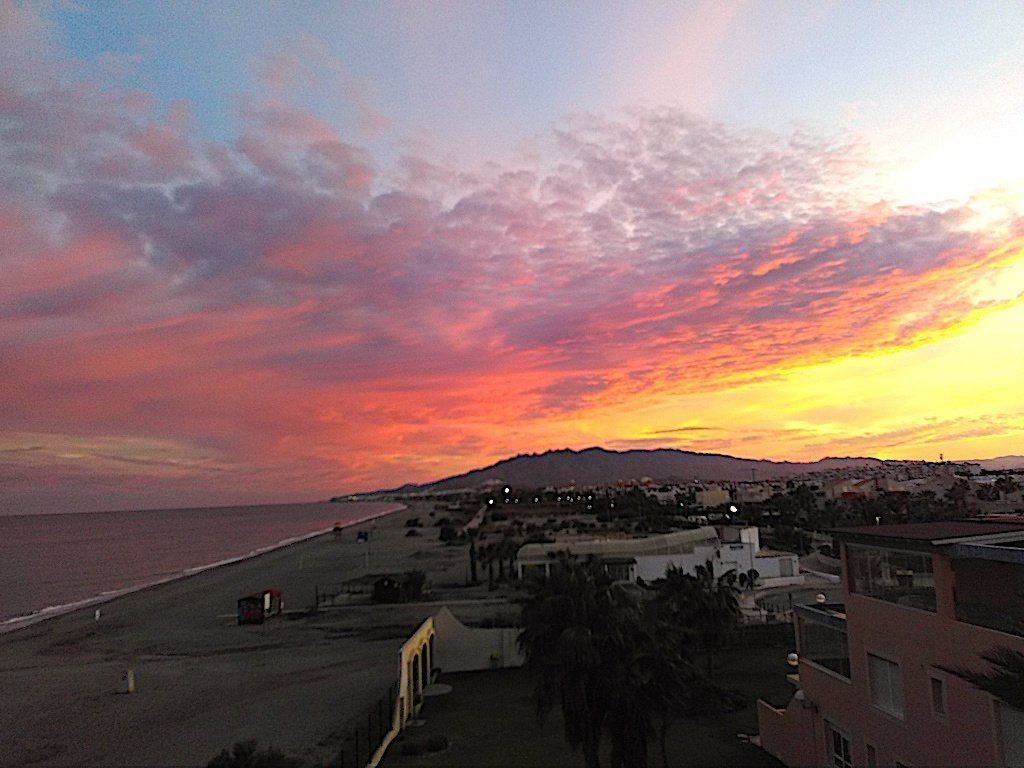 from high up looking right down the beach to the mountains at sunset and the sky is on fire with orange and pink colours