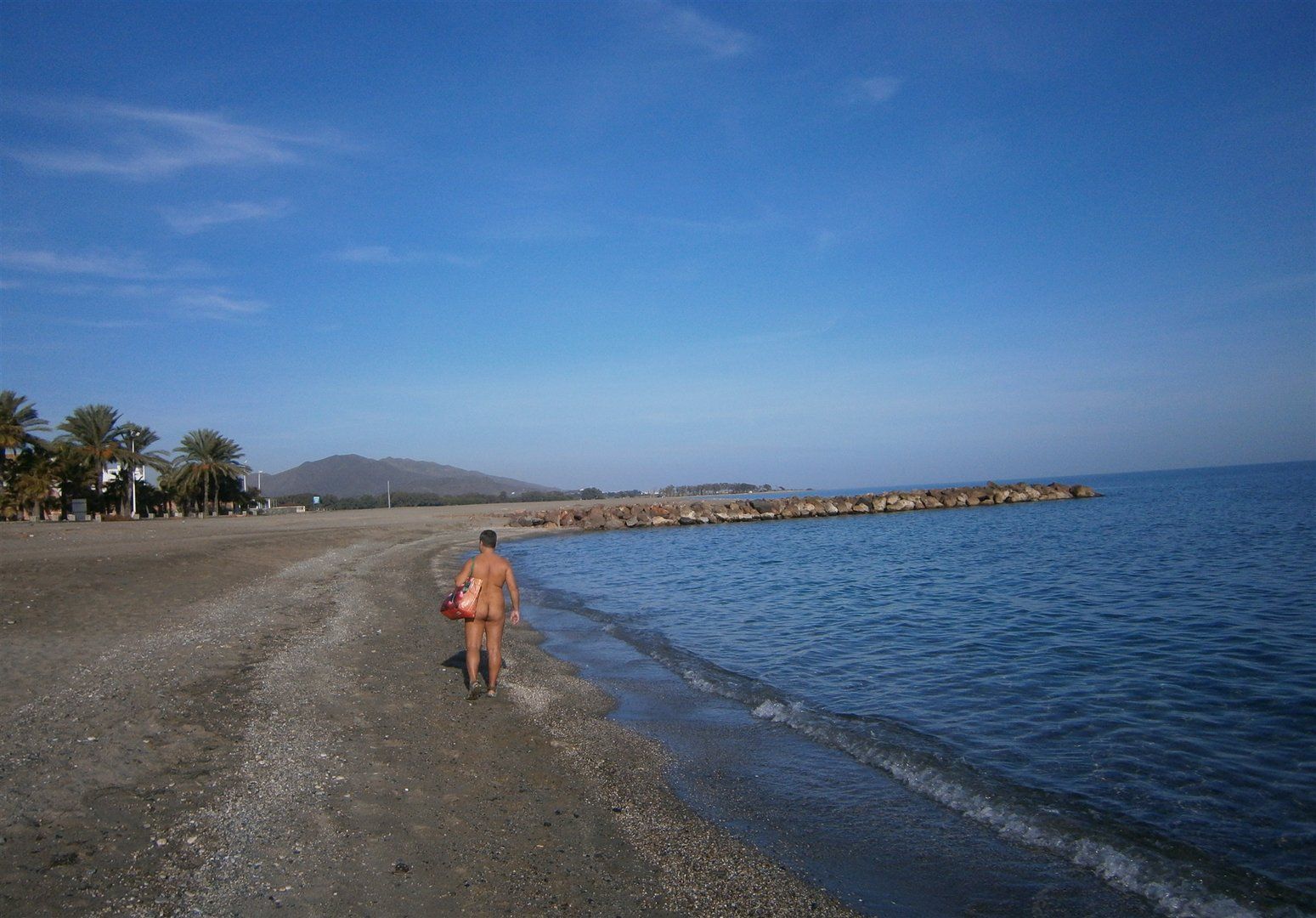 taken from behind a lone person walks naked along the shoreline