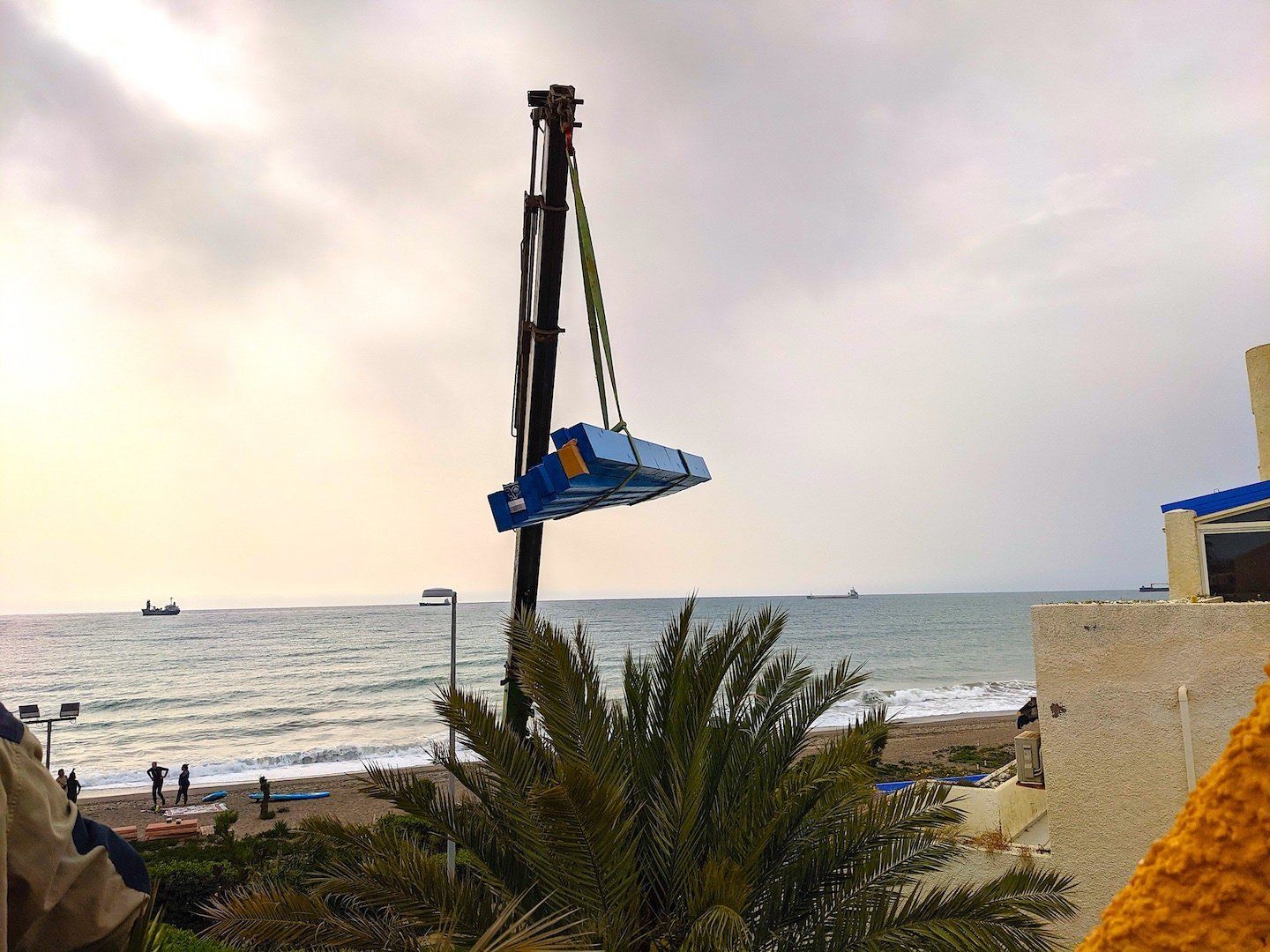 an arm of a crane hoists a load in the air and the sea is in the background