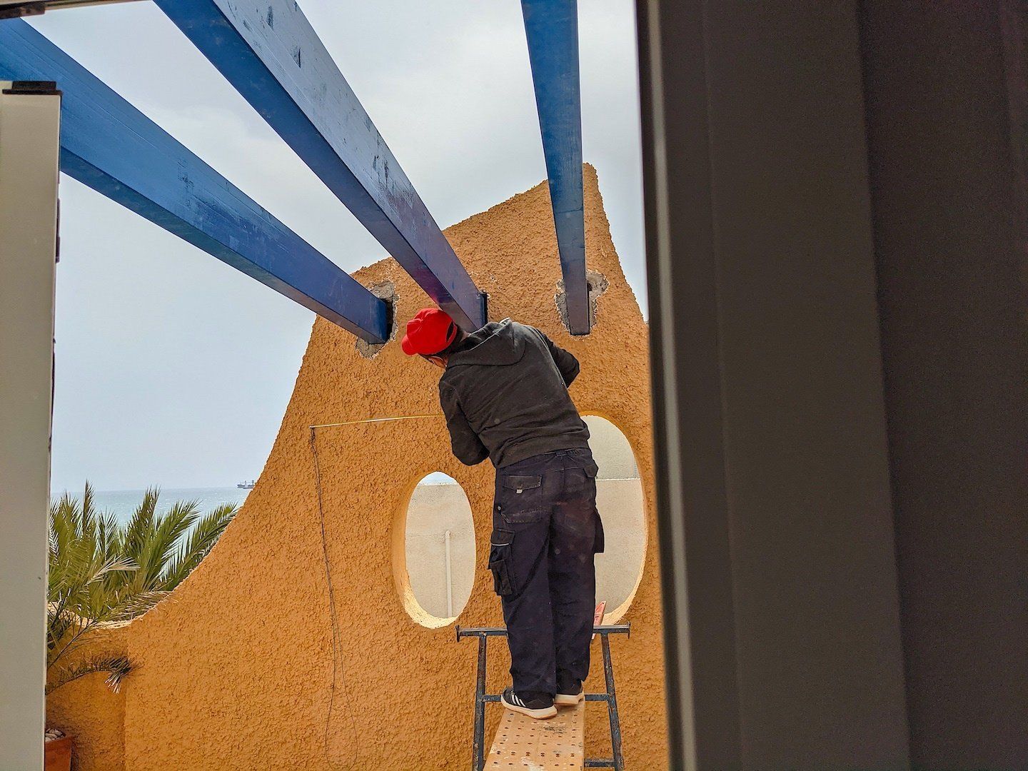 beams in place up above while a workman is stood on a scaffold plank working on them