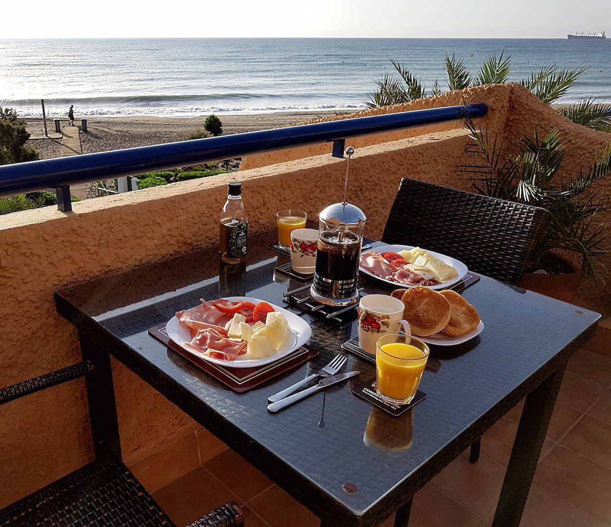 glass top table spread with continental breakfast and coffee with orange juice with the view of the beach beyond