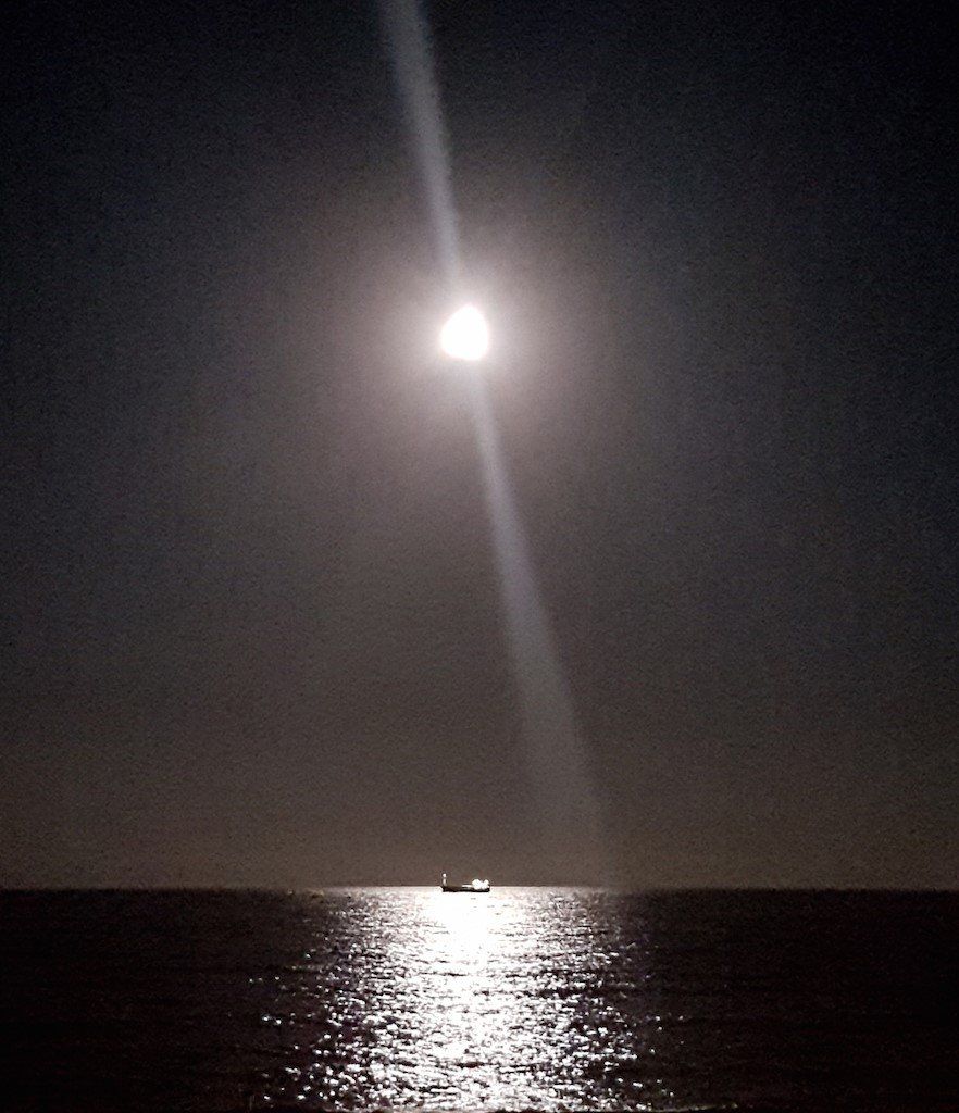 moon high in the sky above vera playa beach casting a beam of light on a boat on the water