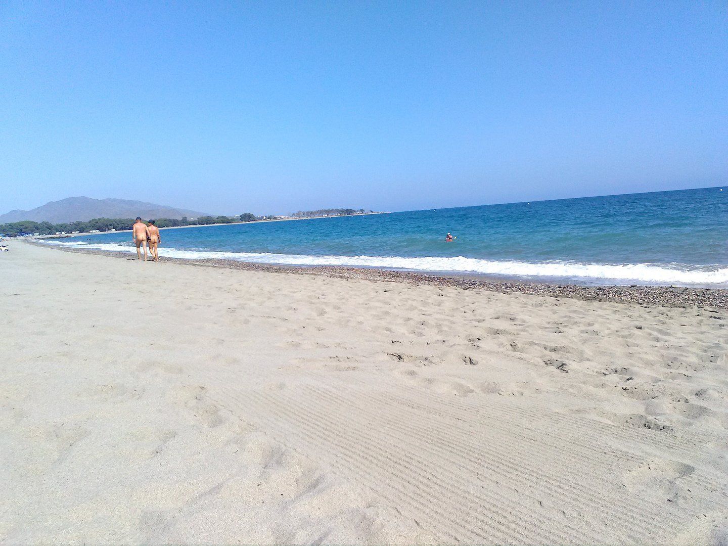 taken from behind a couple walk naked along the shoreline