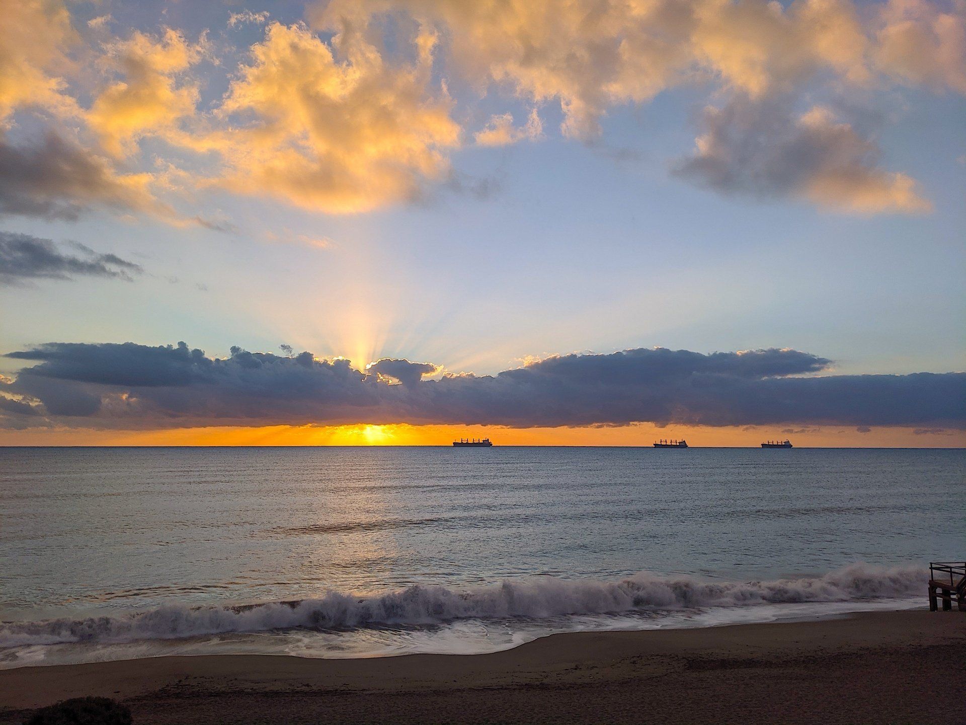 looking out across the sea at dawn with orange and yellow sky and three ships on the horizon