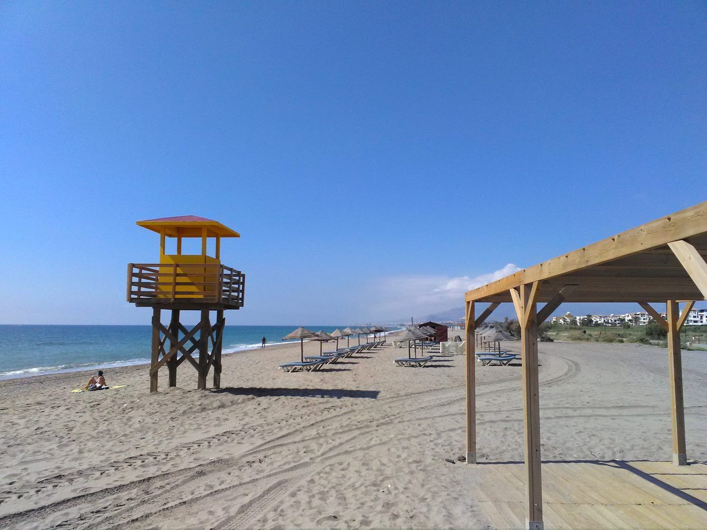 yellow lifeguard tower with rows of empty sunbeds and parasols on a snady beach before the crowds arrive