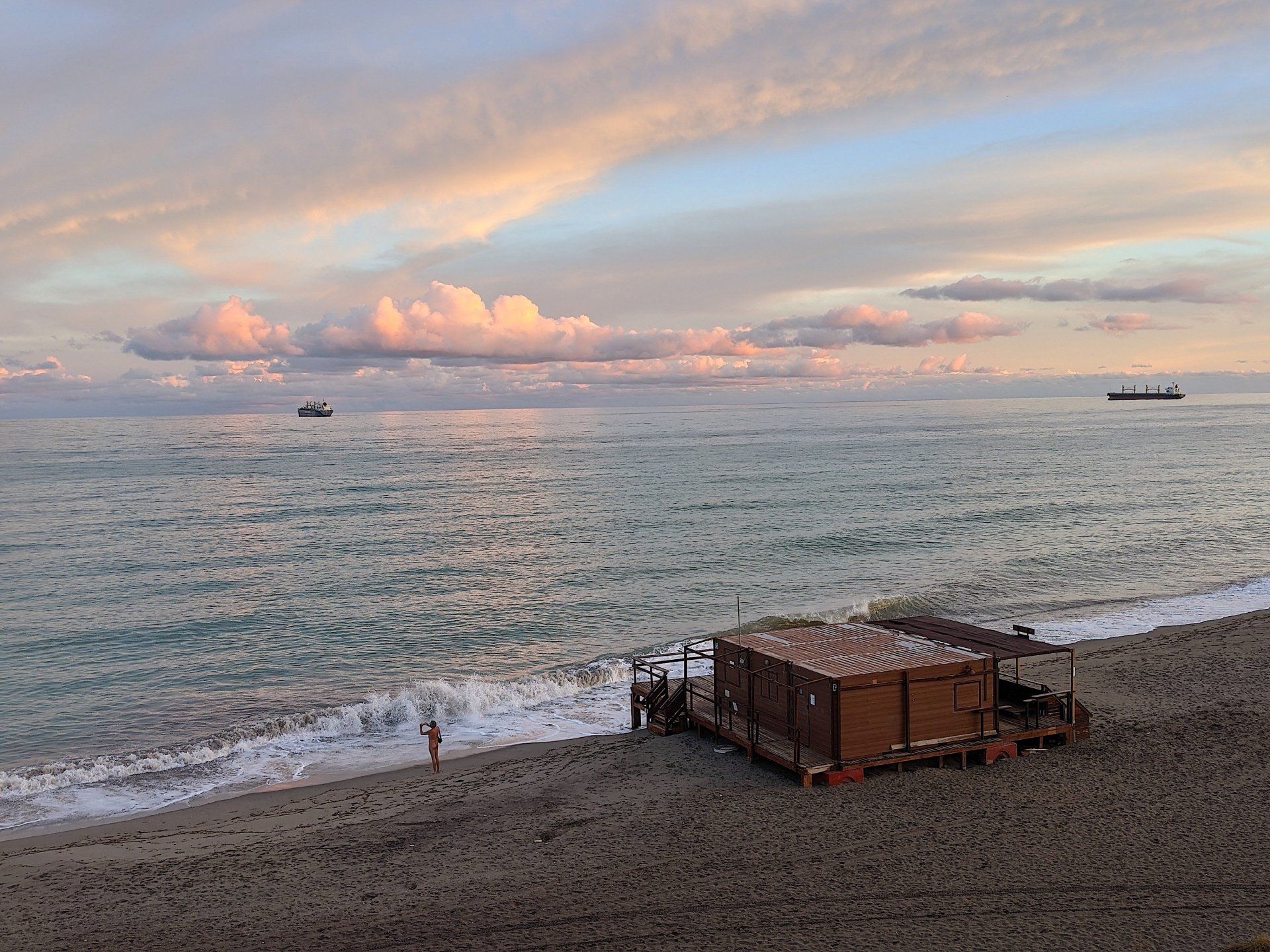 looking down onto the beach and a wooden beach bar at the shoreline and the sea reflects the blue and pink sky at dusk