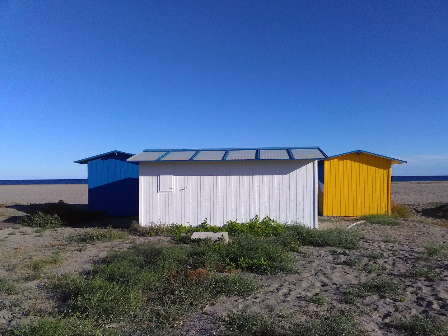 three beach huts in lovely vibrant colours from left blue white and yellow