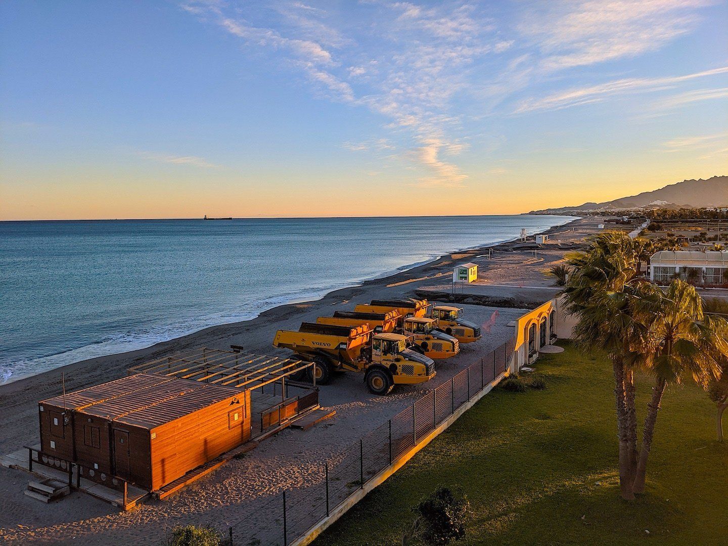 a line up of massive dumper trucks on the beach next to a beach bar all closed up for winter