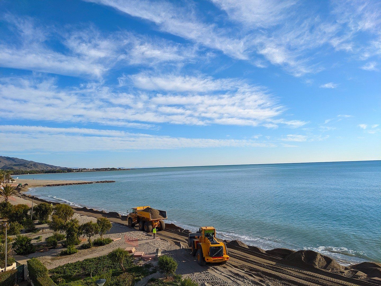 a big commercial dumper and tractor work together on the beach dumping sand and raking it