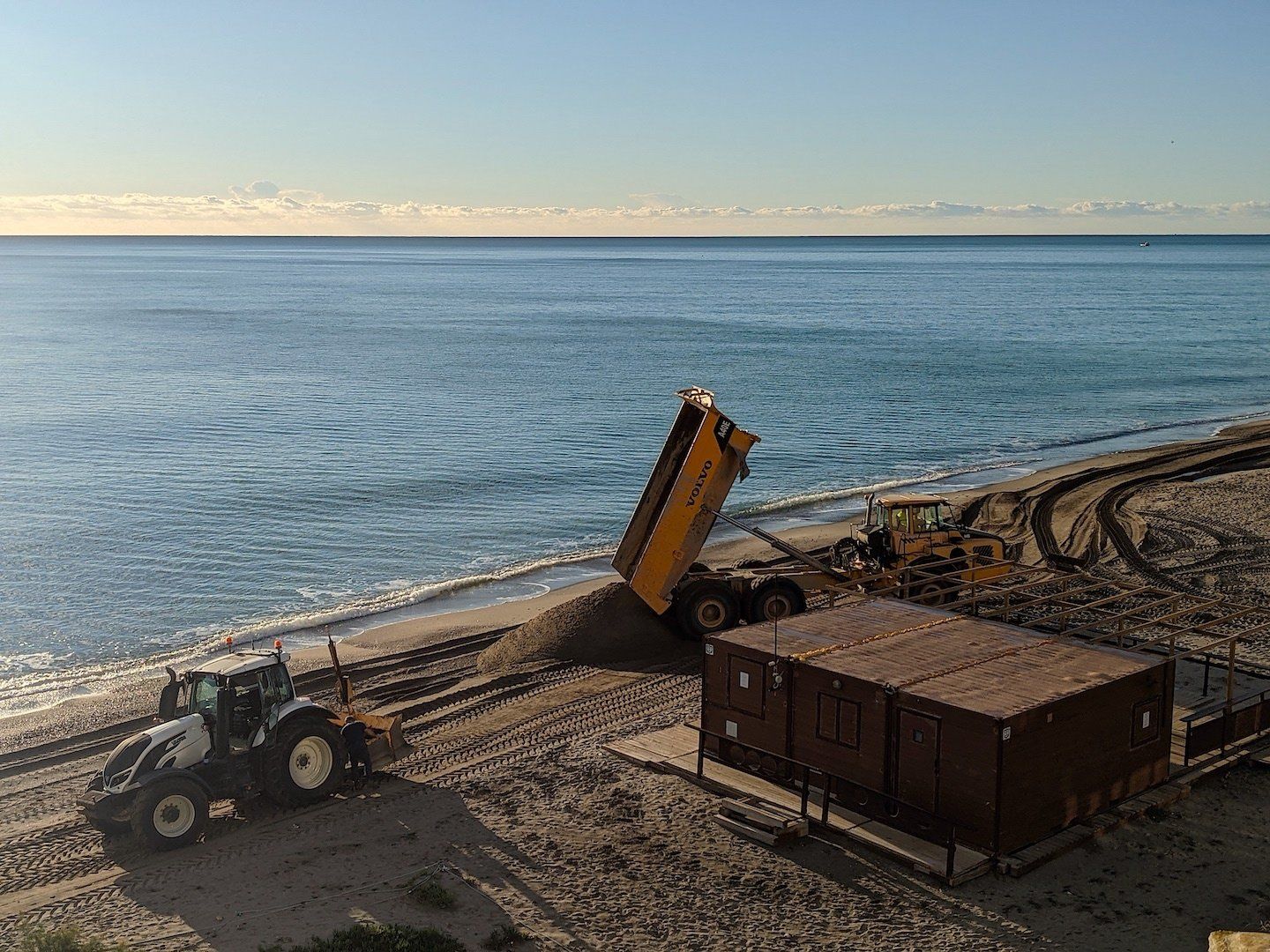 a big commercial dumper dumps sand onto the beach