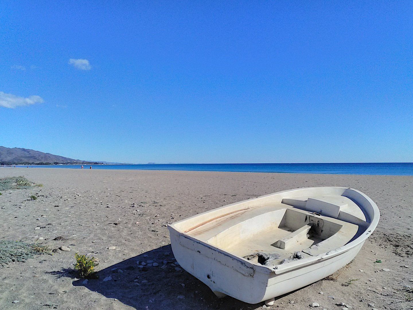on the expanse of sand is a single abandoned looking white rowing boat