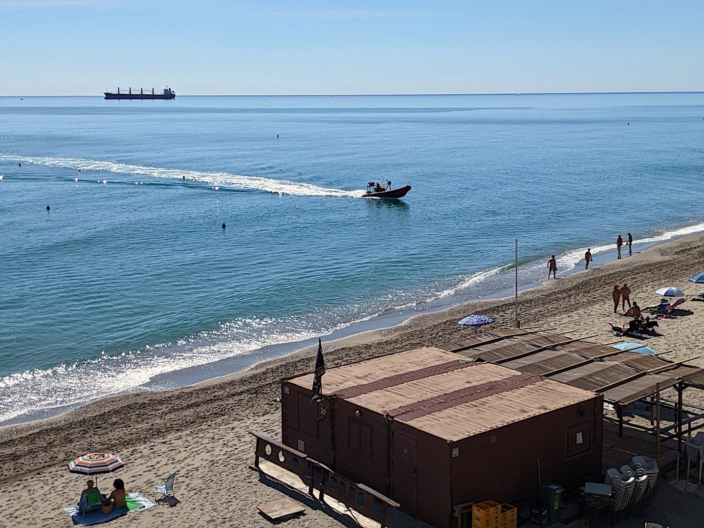 small boat on calm sea with buoys, sandy beach and beach bar