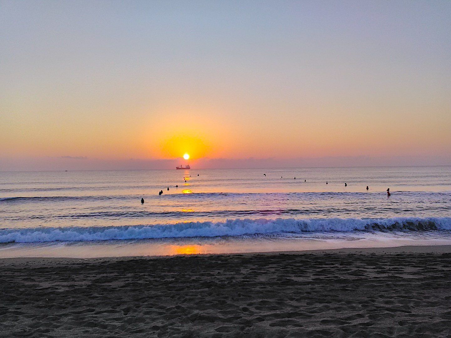 sand and floating buoys in the foreground with a yellow and orange sun on the horizon rising out of the mediterranean