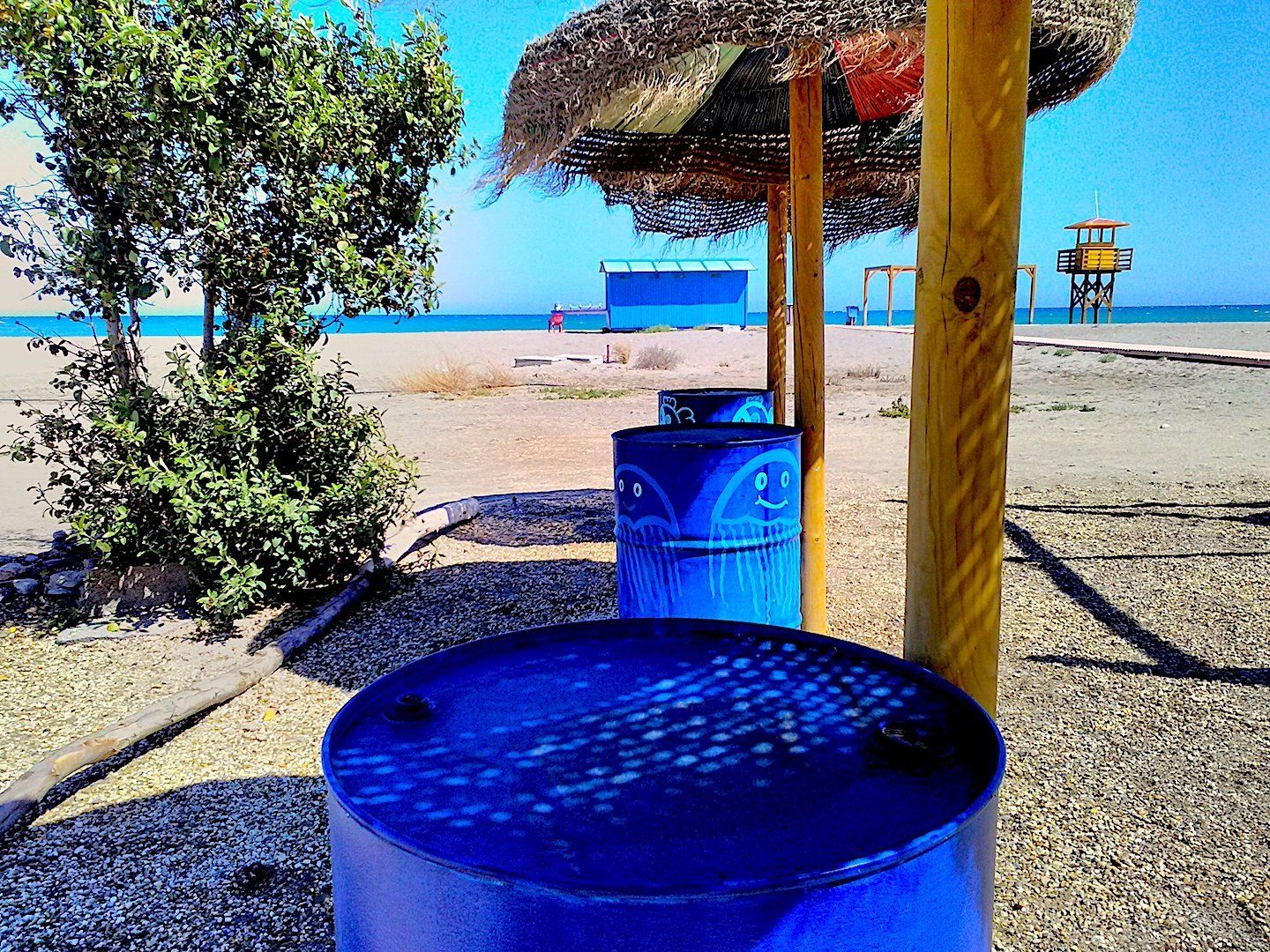 old oil barrels painted bright blue stood next to sun parasols acting like bar tables