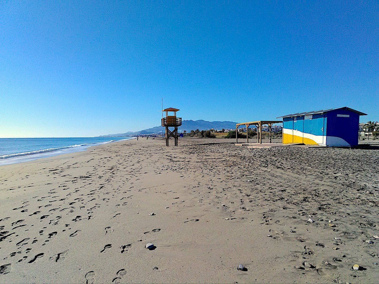 a quiet beach with a lifeguard tower and hut but there are plenty of footsteps in the sand