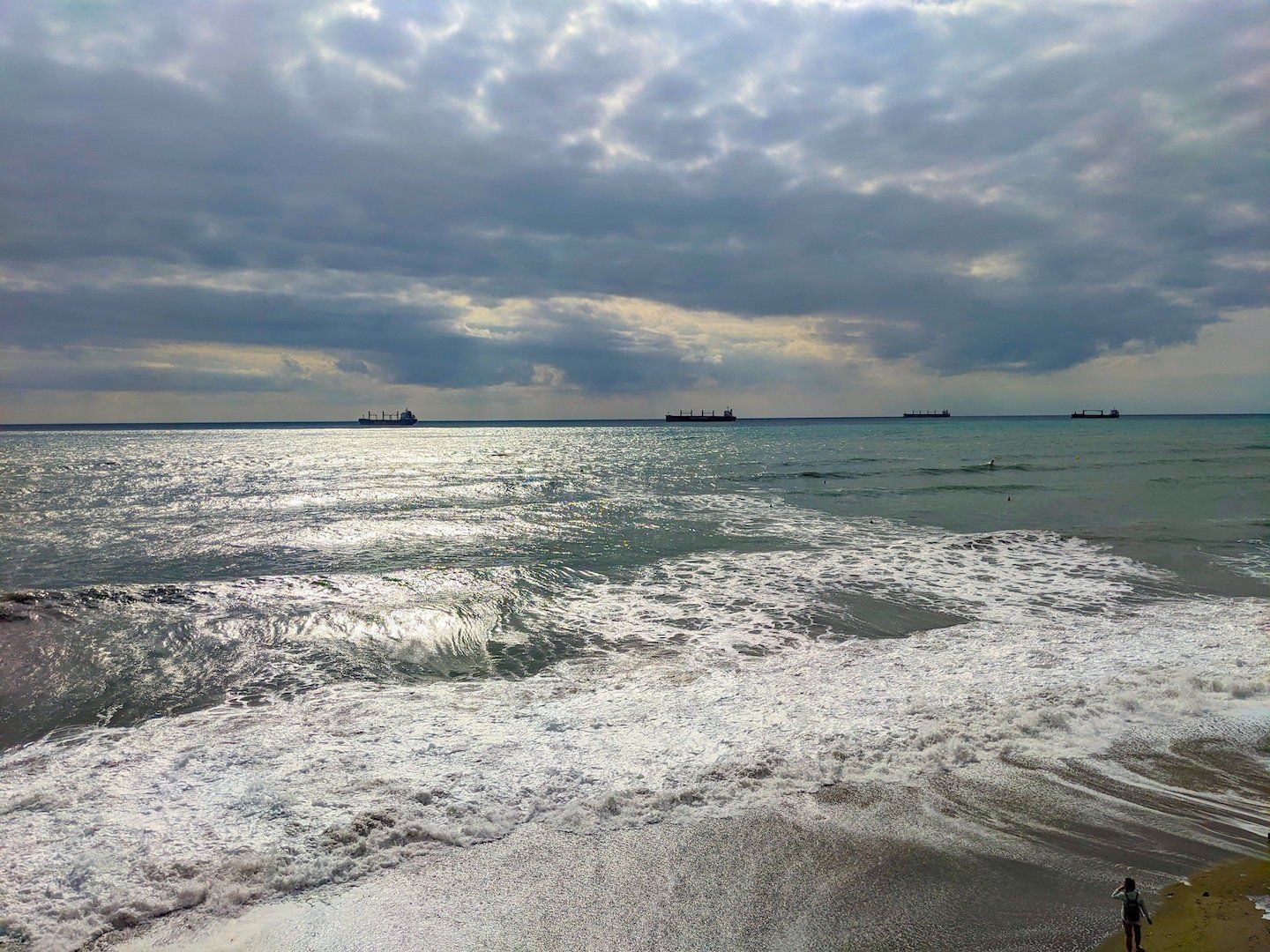rough sea, 4 ships, sandy beach with a person watching from shore