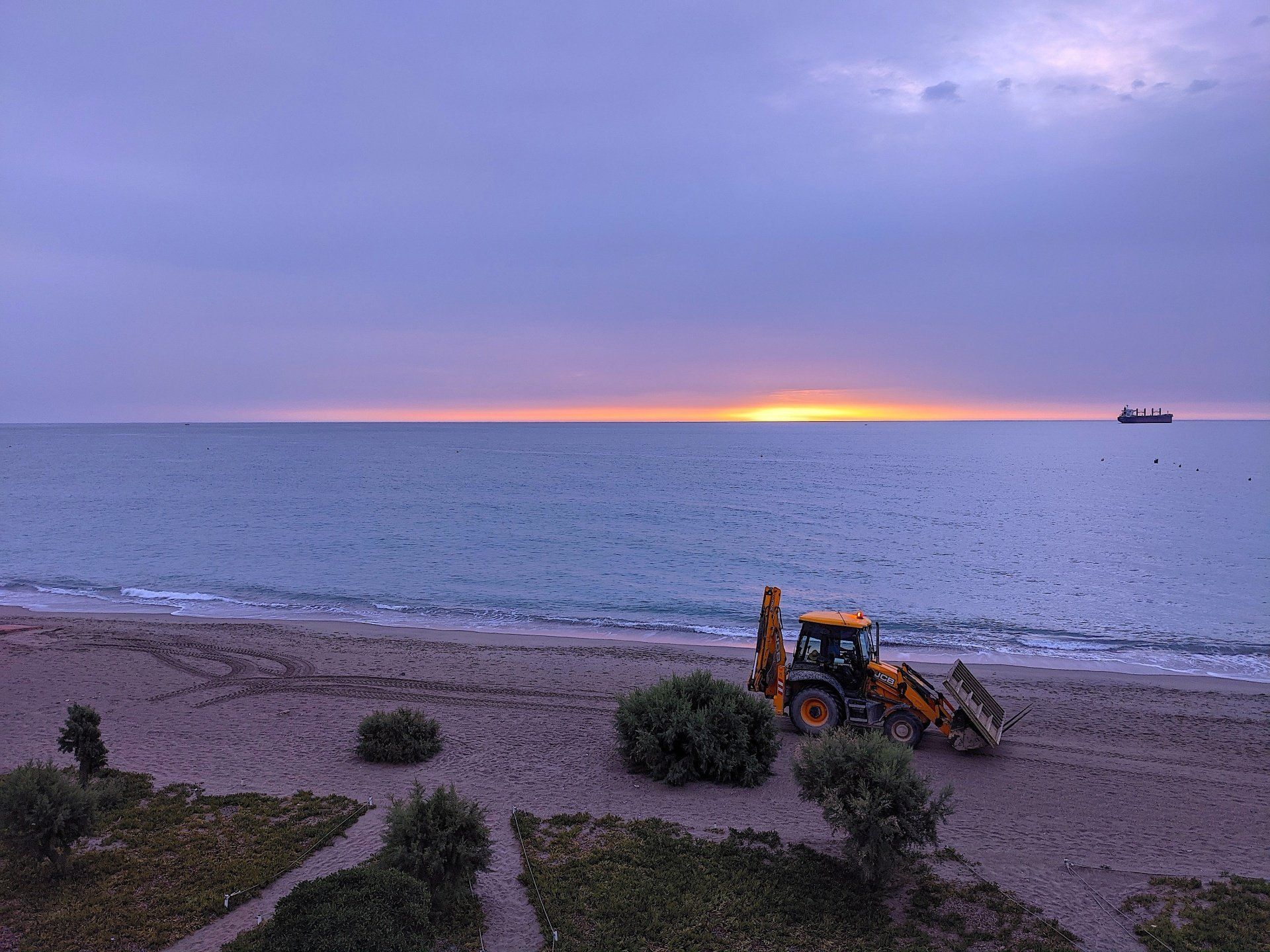 tractor on sand driving away with section of concrete path in the front bucket