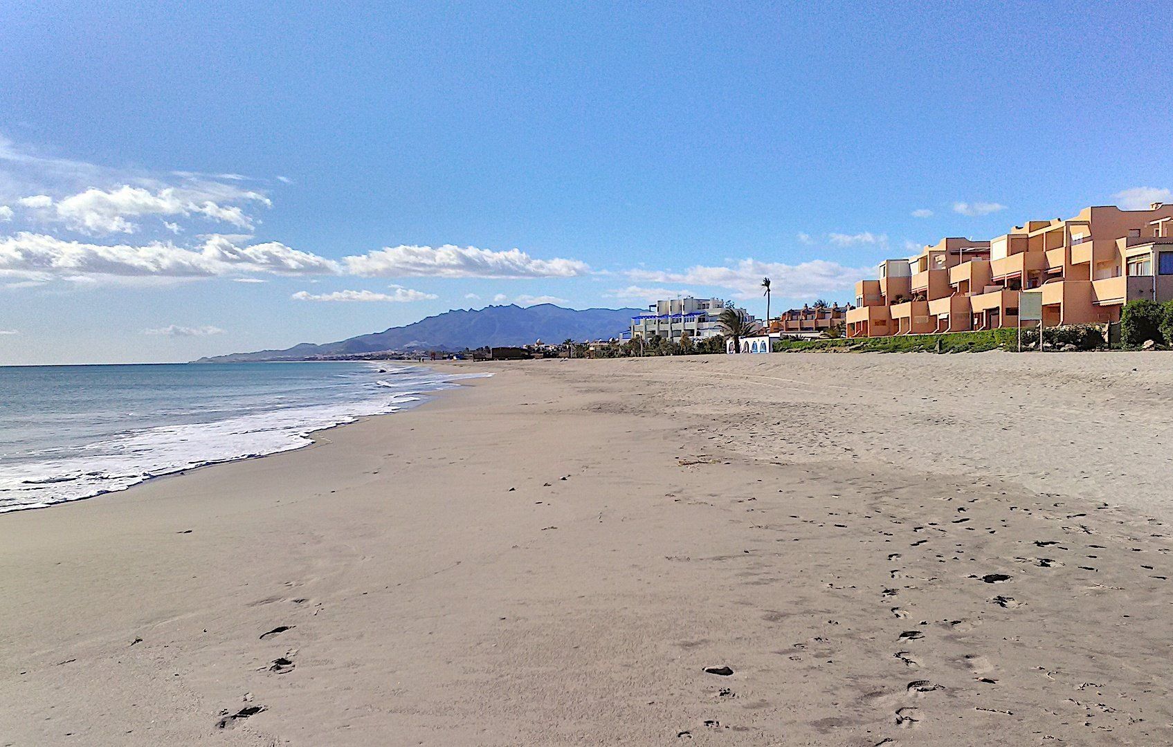 lovely smooth sand going down to the shore while on the left are apartments on the beach