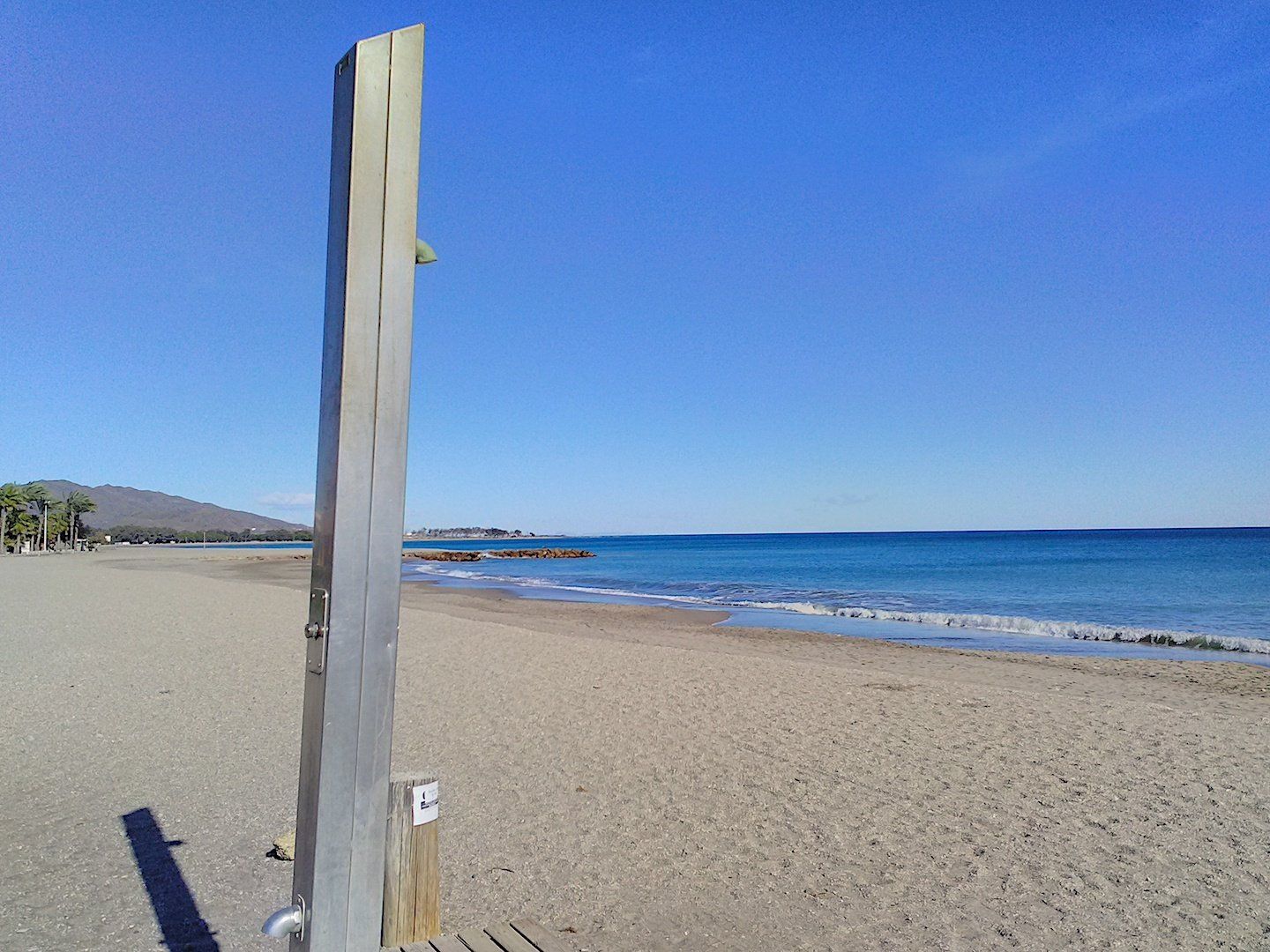 a single metal shower on the sand looking out to sea