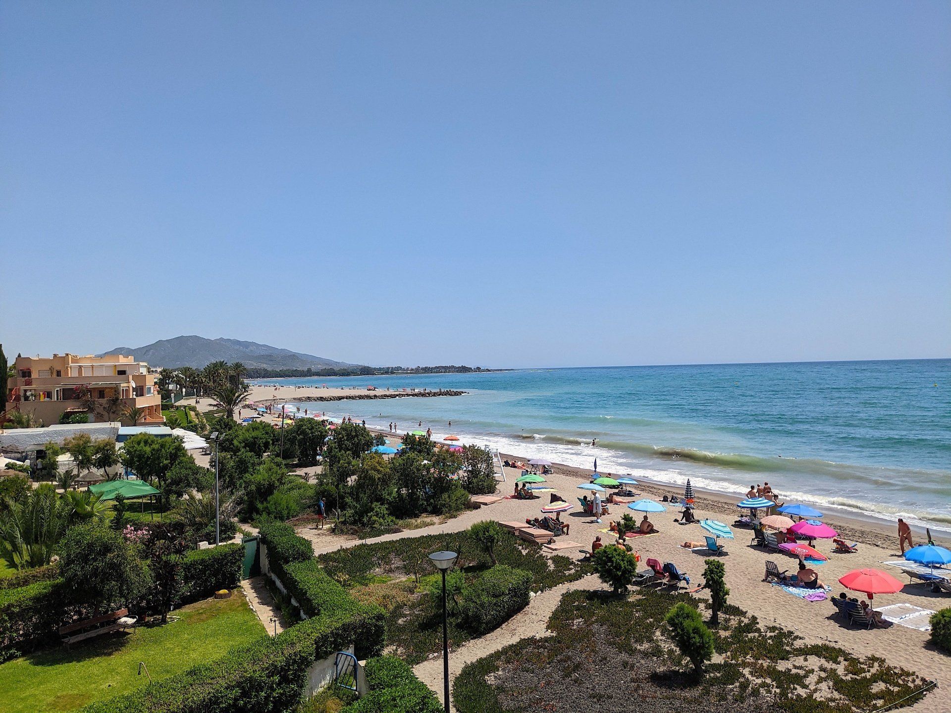 looking down onto the beach from above on a hot sunny day and sunbathers with sun umbrellas are relaxing on the sand