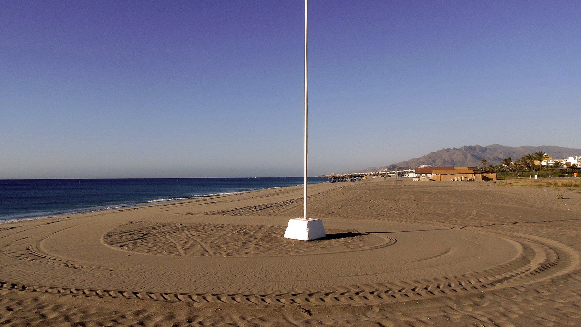 a close up of a single flag pole on freshly raked sand with the rest of the beach in the background