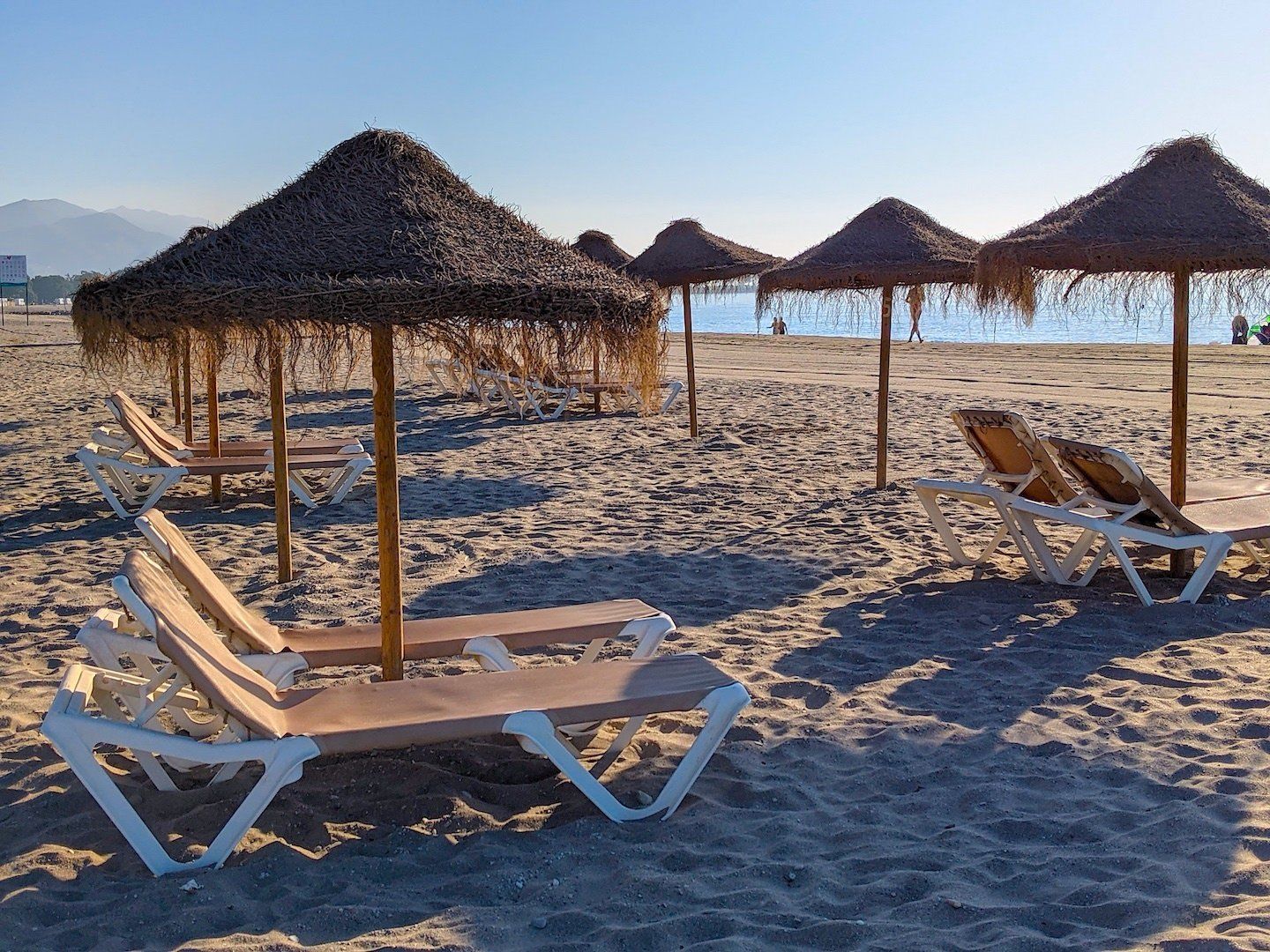 close up of straw sun umbrellas and sun loungers on a deserted sandy beach