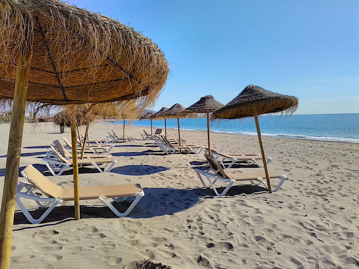 Sombrillas de paja en la playa de arena con costa en frente