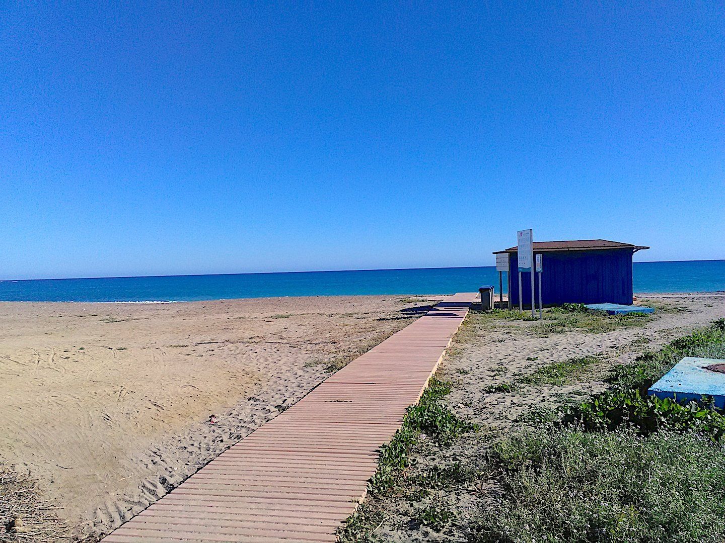 boardwalk style walkway across the sand leading to a little blue wooden hut