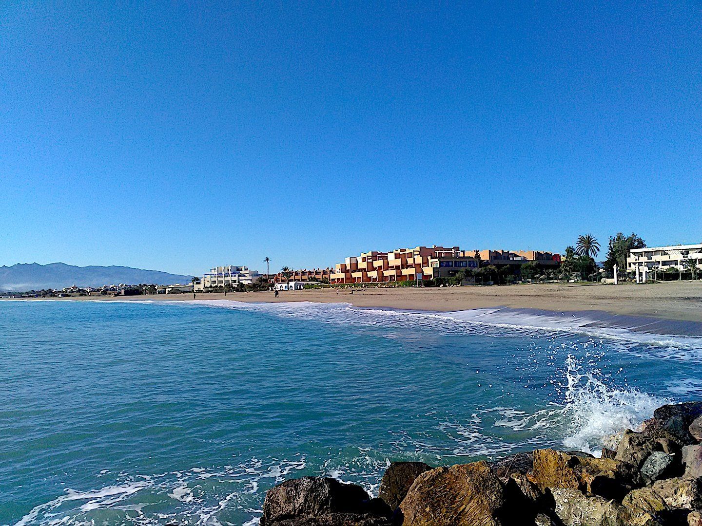 wide view of the bay over the water with sea splashing against the rocks in the foreground