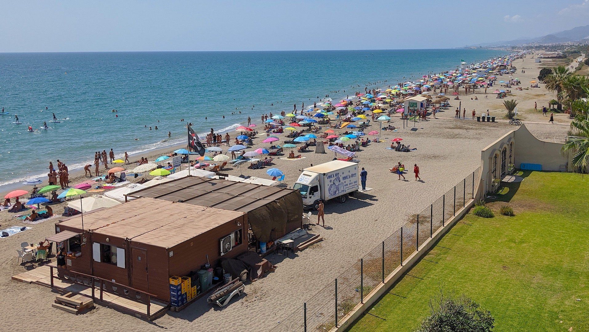 beach bar on a hot summer day with a van parked on the sand and lots of colourful sun umbrellas can be seen for miles
