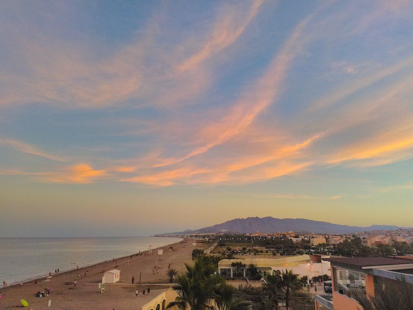 from high looking over the tops of palm trees with the beach stretching away to the mountains in the distance at sunset with pink clouds high in the sky