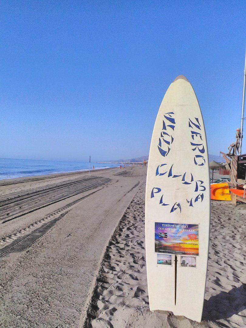 a surf board stands upright in the sand and is used as an advertising board at the pirate bar looking southwards