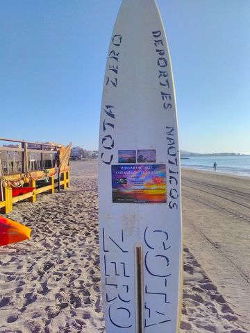 a surf board stands upright in the sand and is used as an advertising board at the pirate bar looking northwards