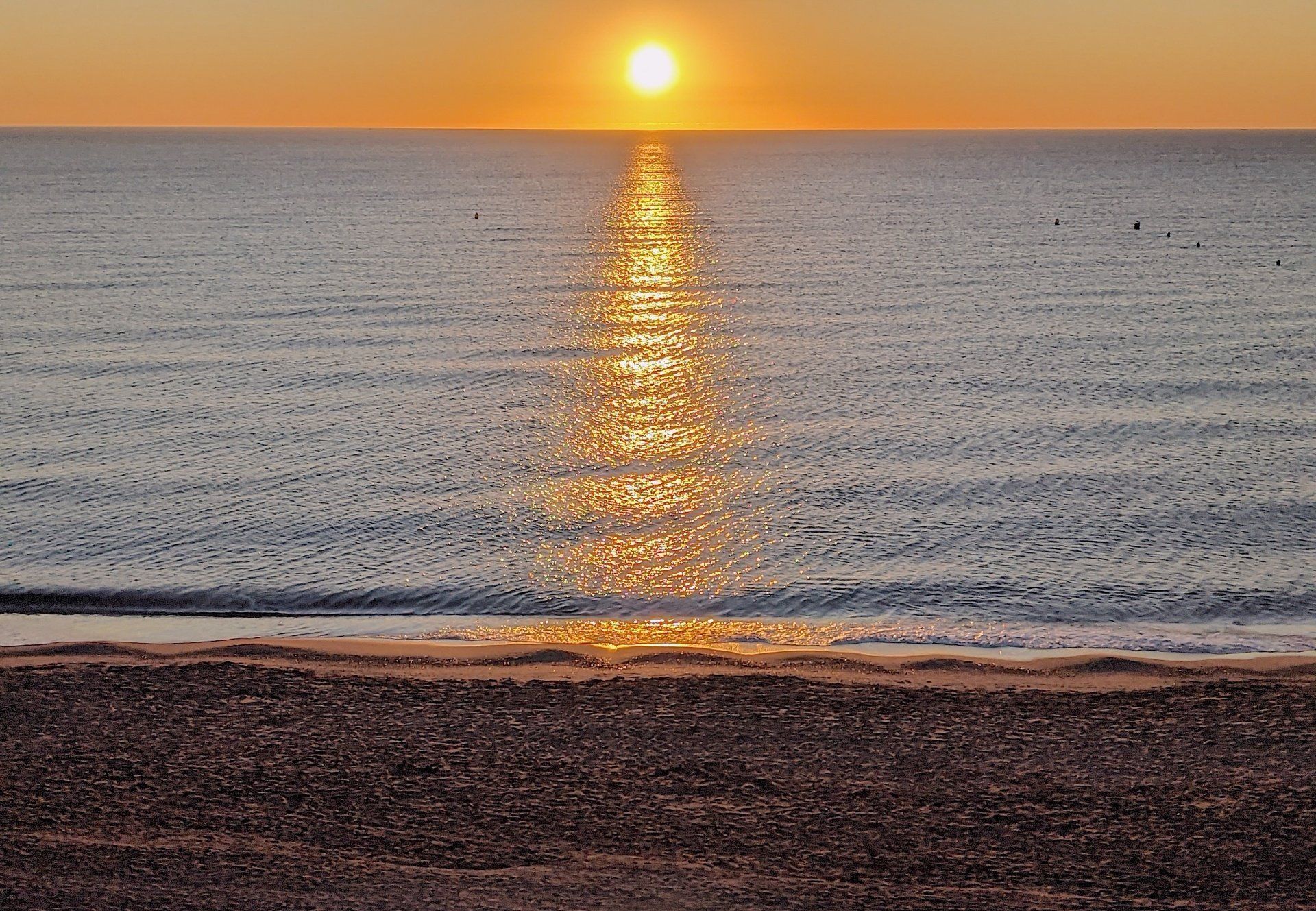 taken from the shoreline the sun rises on the horizon and sends a bolt of orange across the sea