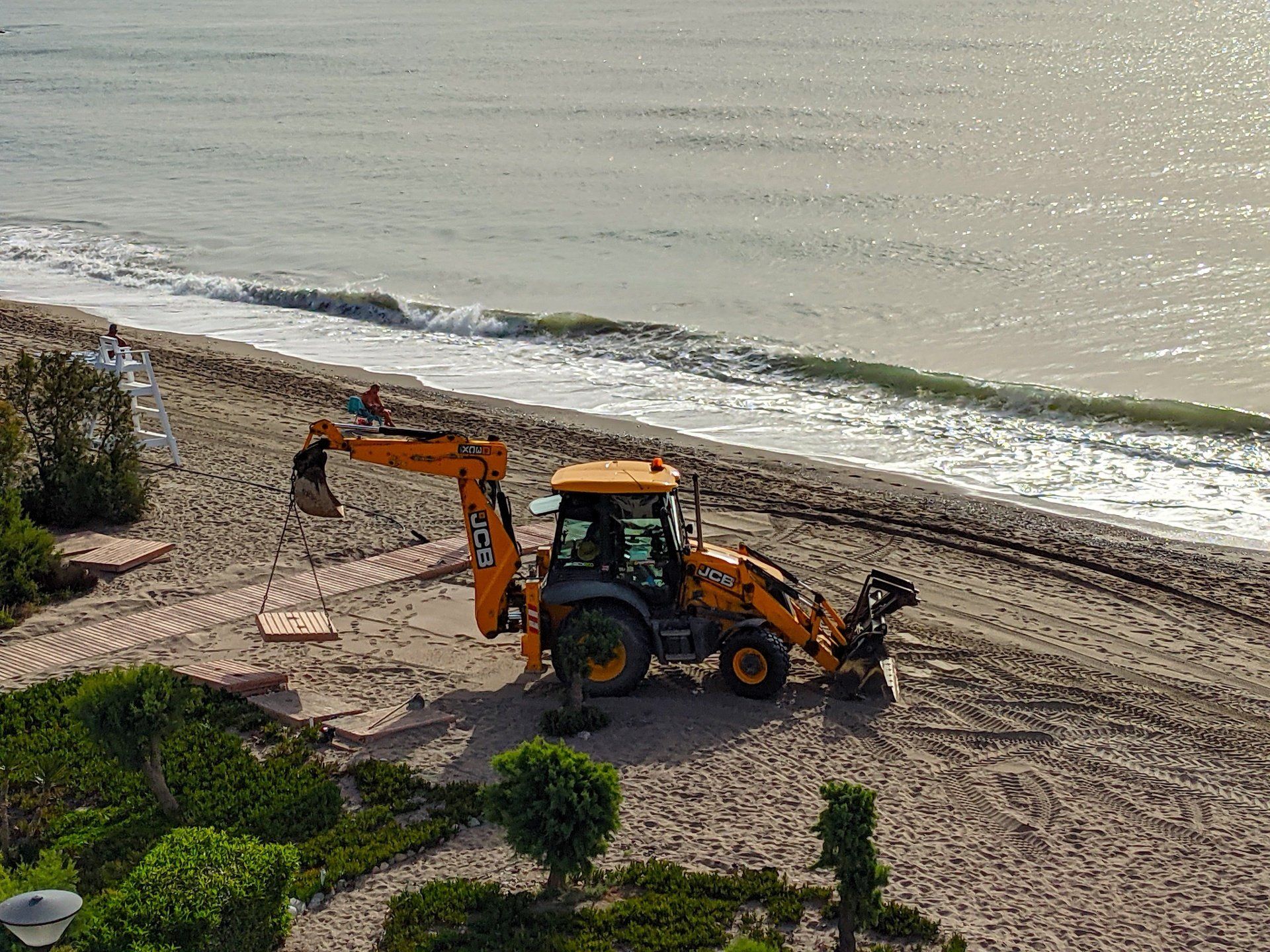 a big yellow tractor carries a section of path into place on the beach