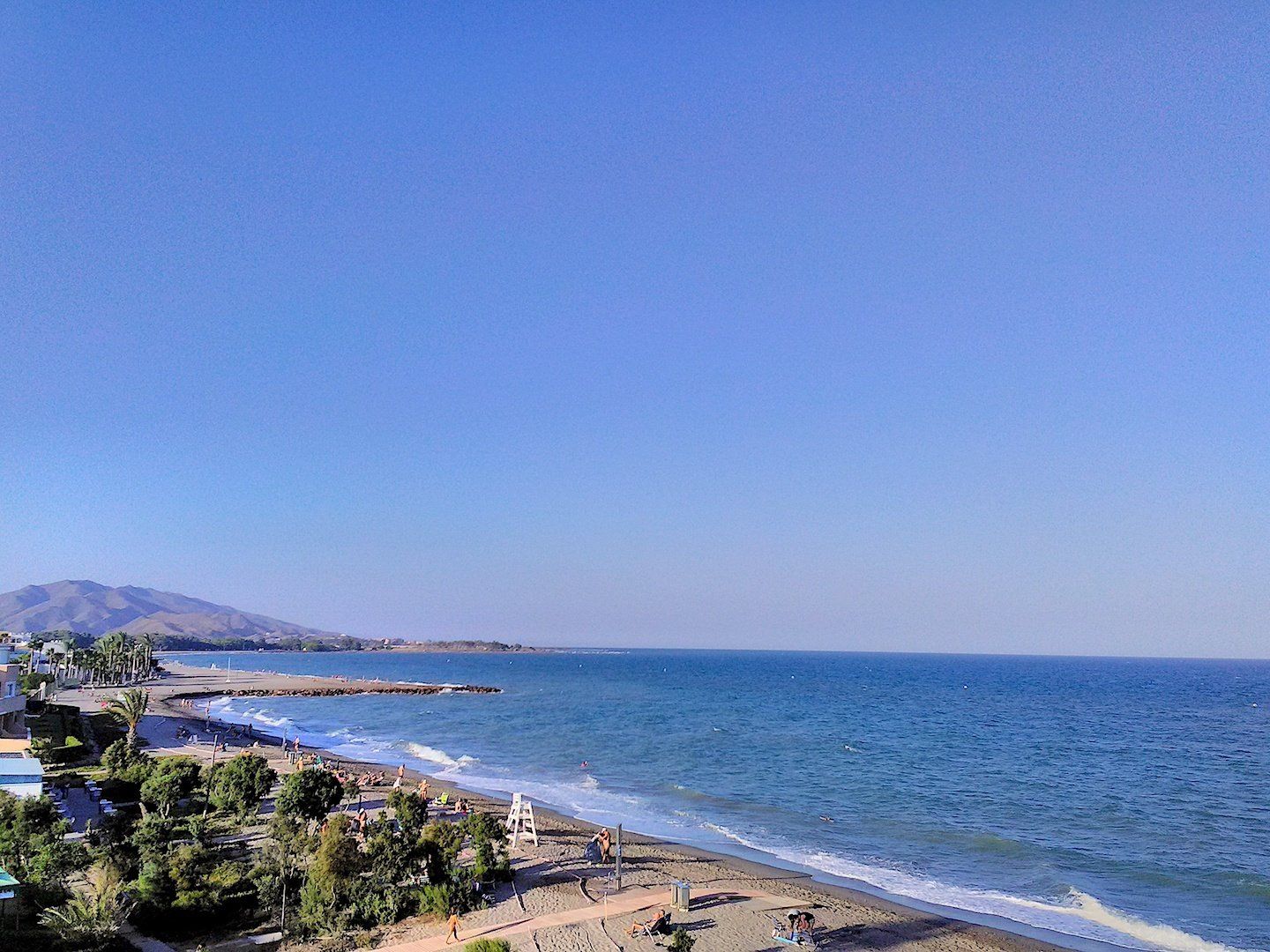 looking north up the beach and twinkling sea and blue skies with mountains in the distance