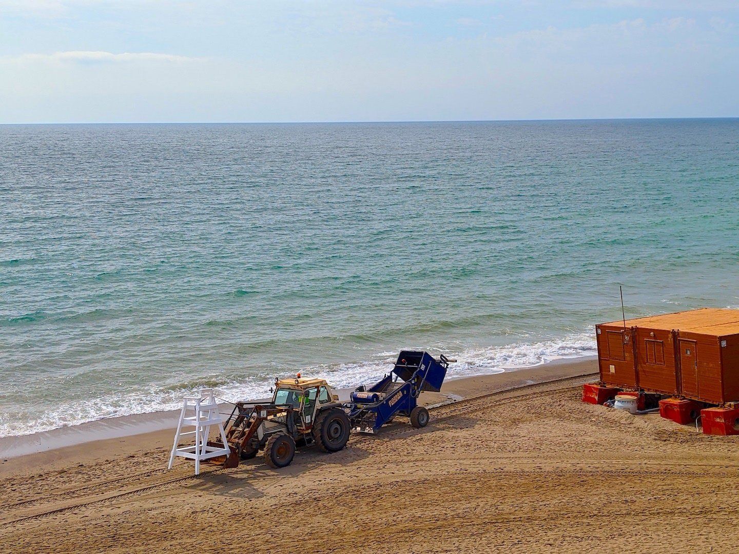 a big tractor carries a lifeguard tower on its front forks into place across the beach