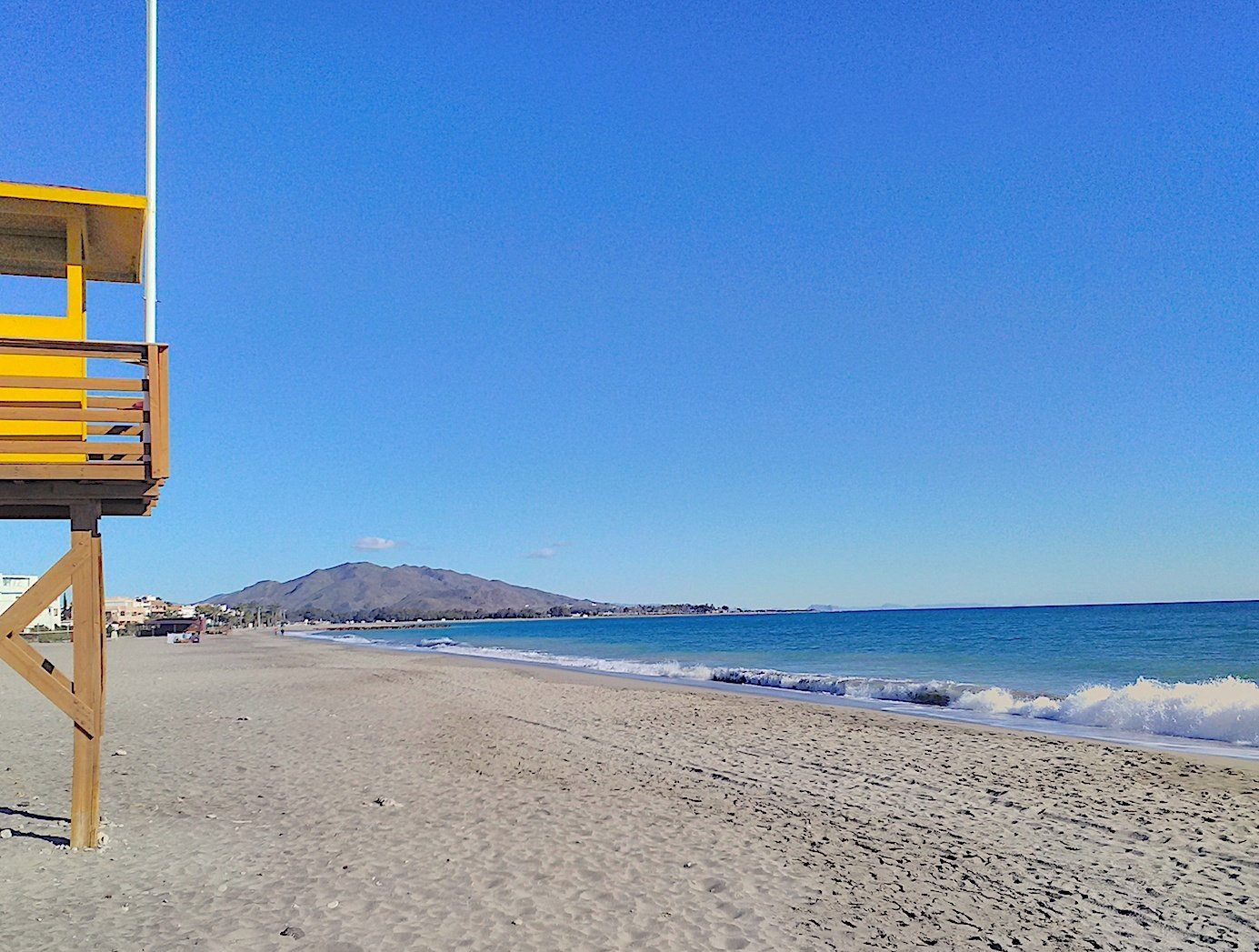 the famous yellow vera playa lifeguard tower partly visible on the left with the sweep of the bay behind it