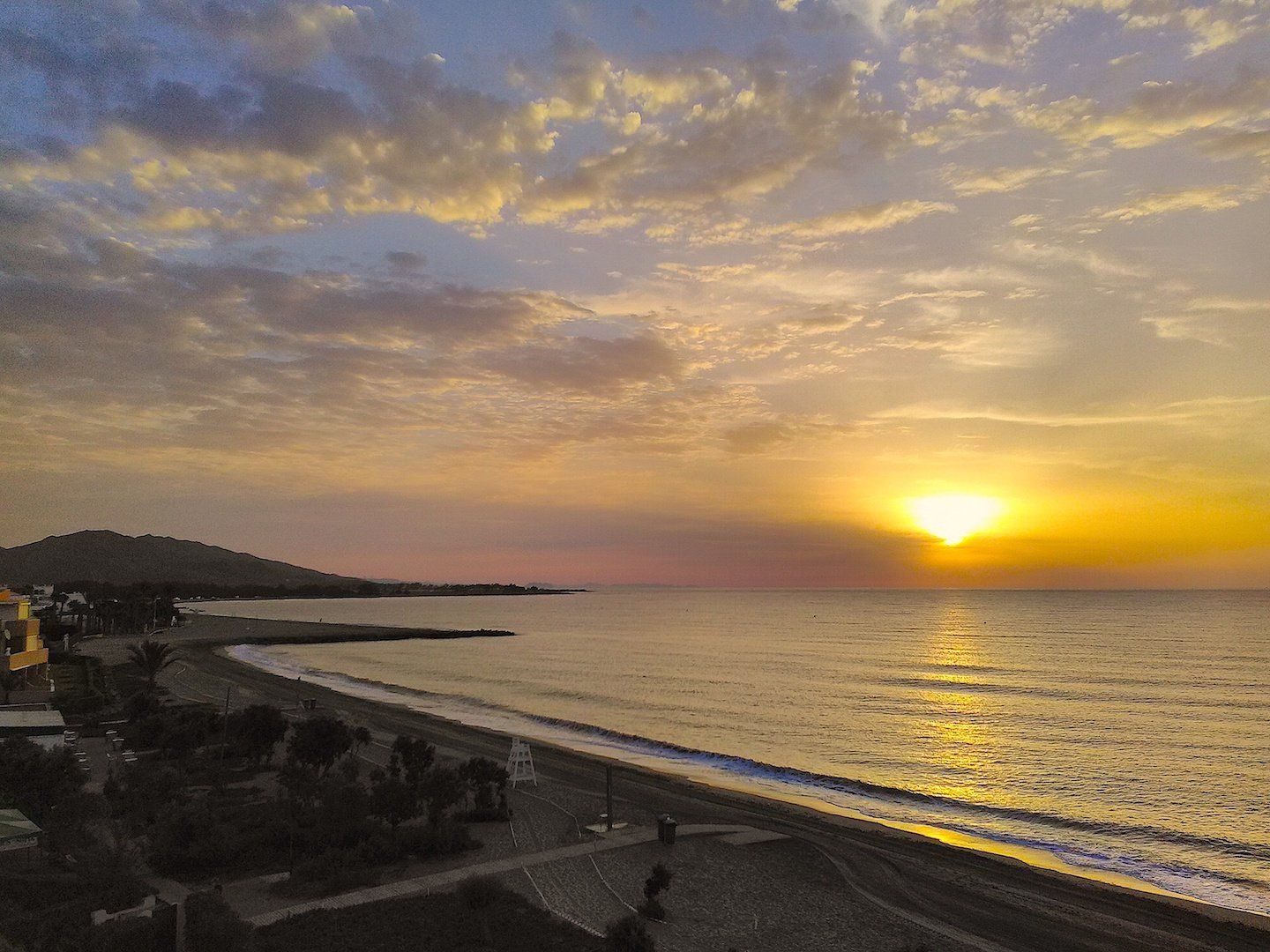 same view as previous but taken at dawn and the sun is rising out the sea lighting the clouds and giving a yellow beam across the sea