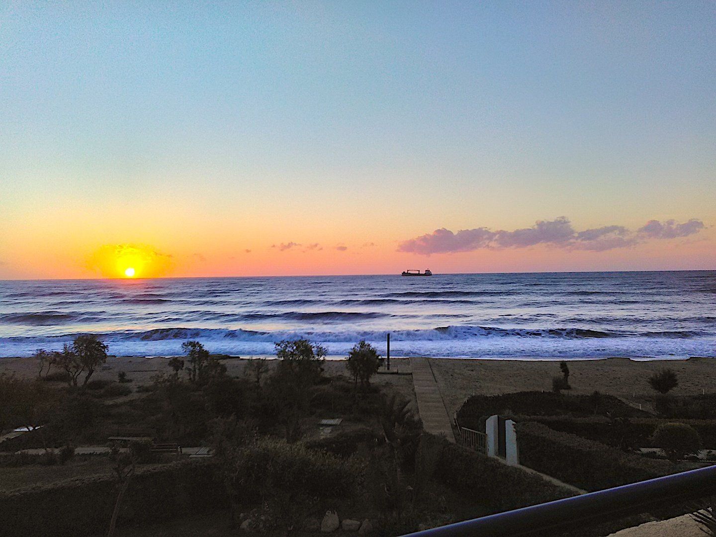 a lively looking sea with an orange sun on the horizon and a ship centre stage